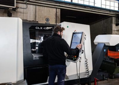 Operatore che gestisce il tornio tramite il pannello di controllo, assicurando precisione nella lavorazione del componente metallico.